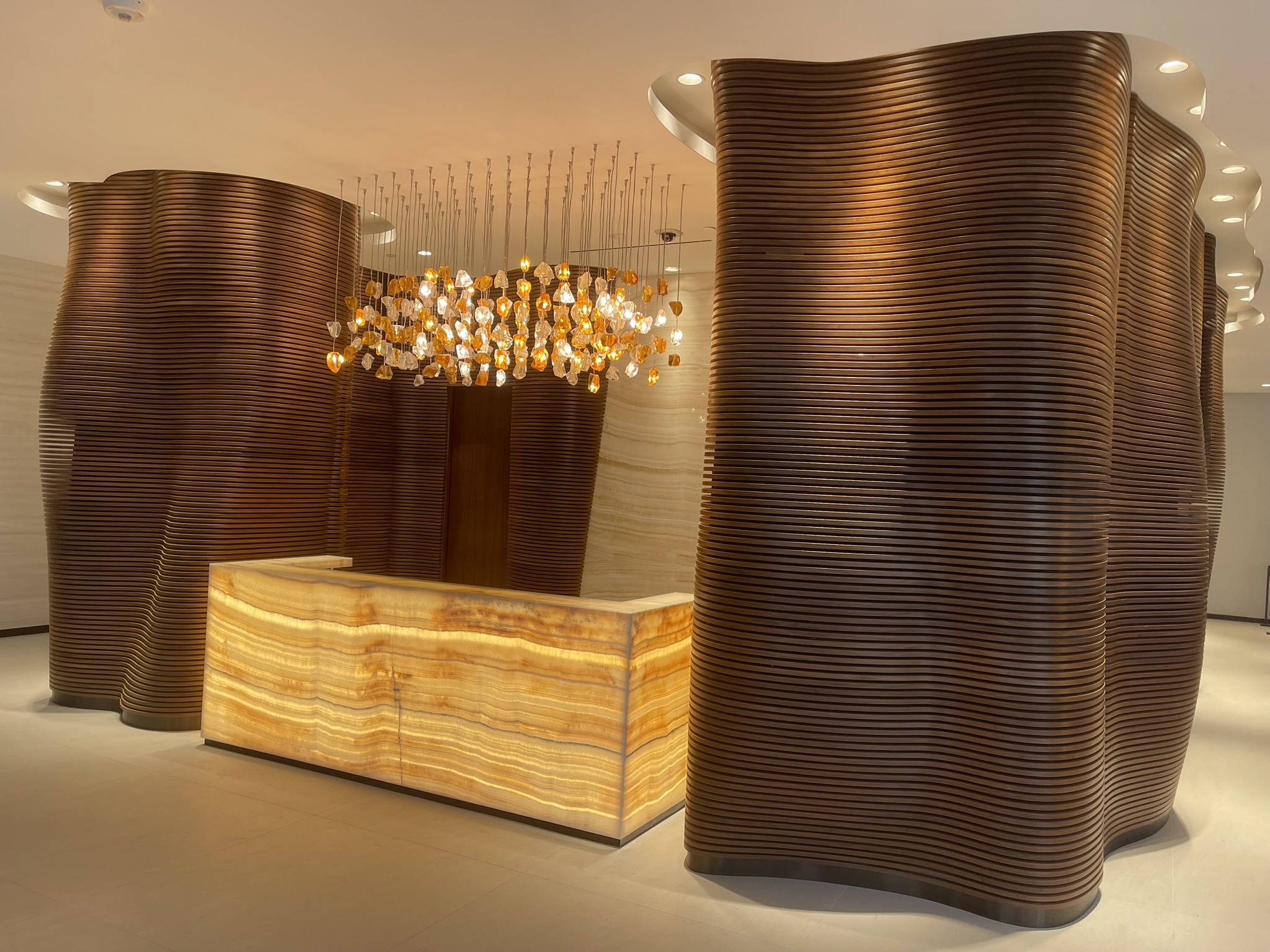 Commercial reception with illuminated onyx desk and sculptural wood wall panels